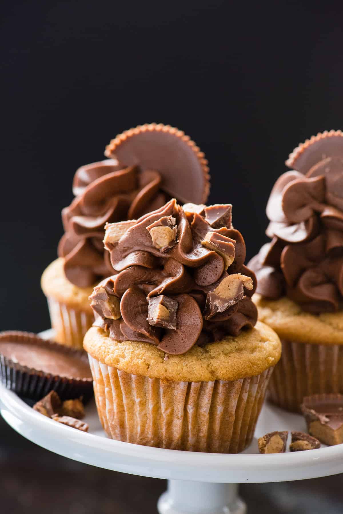 three peanut butter chocolate cupcakes on gray cake stand on black background