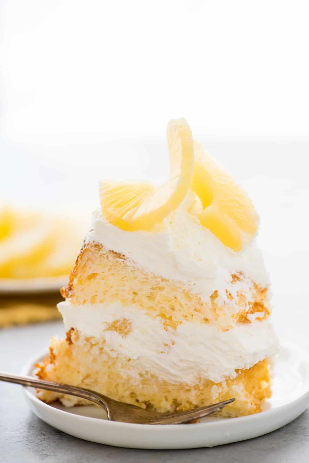 slice of pineapple angel food cake with whipped cream and pineapple on white plate on white background