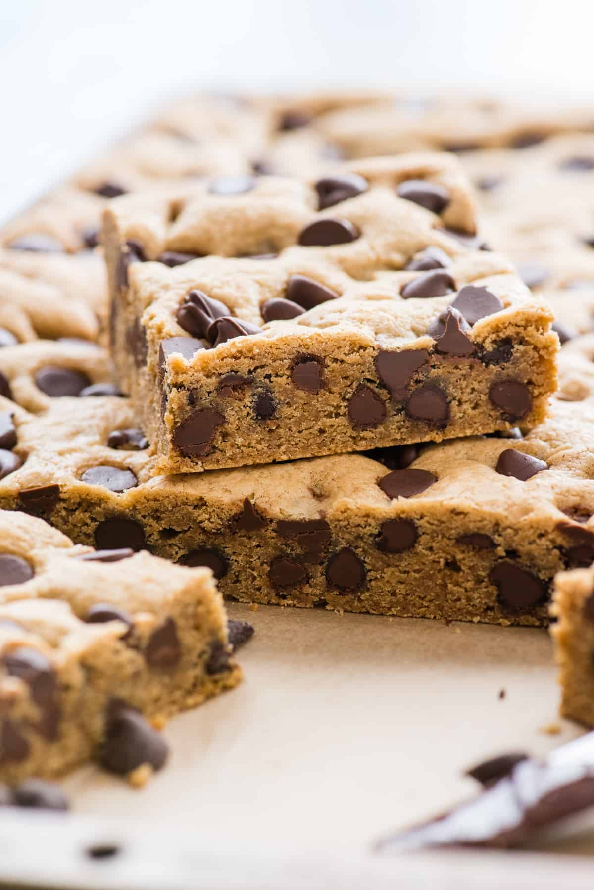 chocolate chip cookie bars in baking sheet with one cookie cut into a square on top of the others