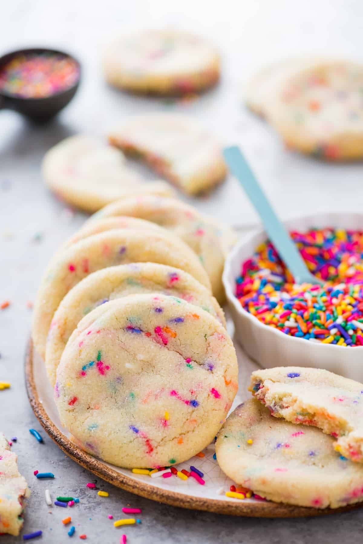 sprinkle cookies arranged in white plate with a container of rainbow sprinkles in the background
