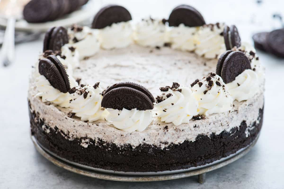 whole no bake oreo cheesecake topped with whipped cream swirls and oreo pieces on white background