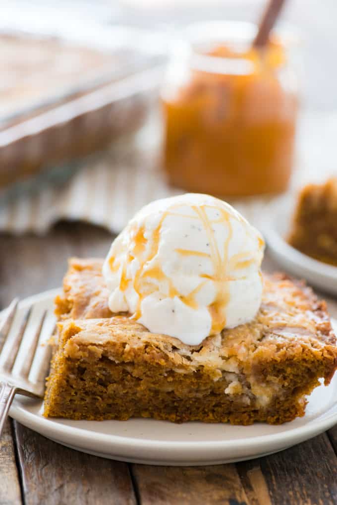 Slice of pumpkin earthquake cake on white plate with scoop of vanilla ice cream on top
