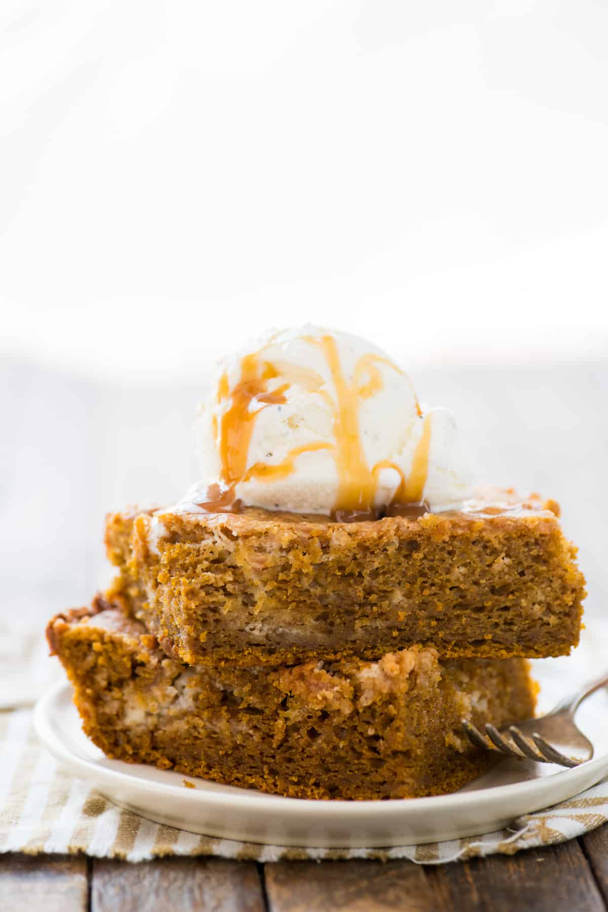 Two slices of pumpkin earthquake cake stacked on top of each other on white plate with scoop of vanilla ice cream on top