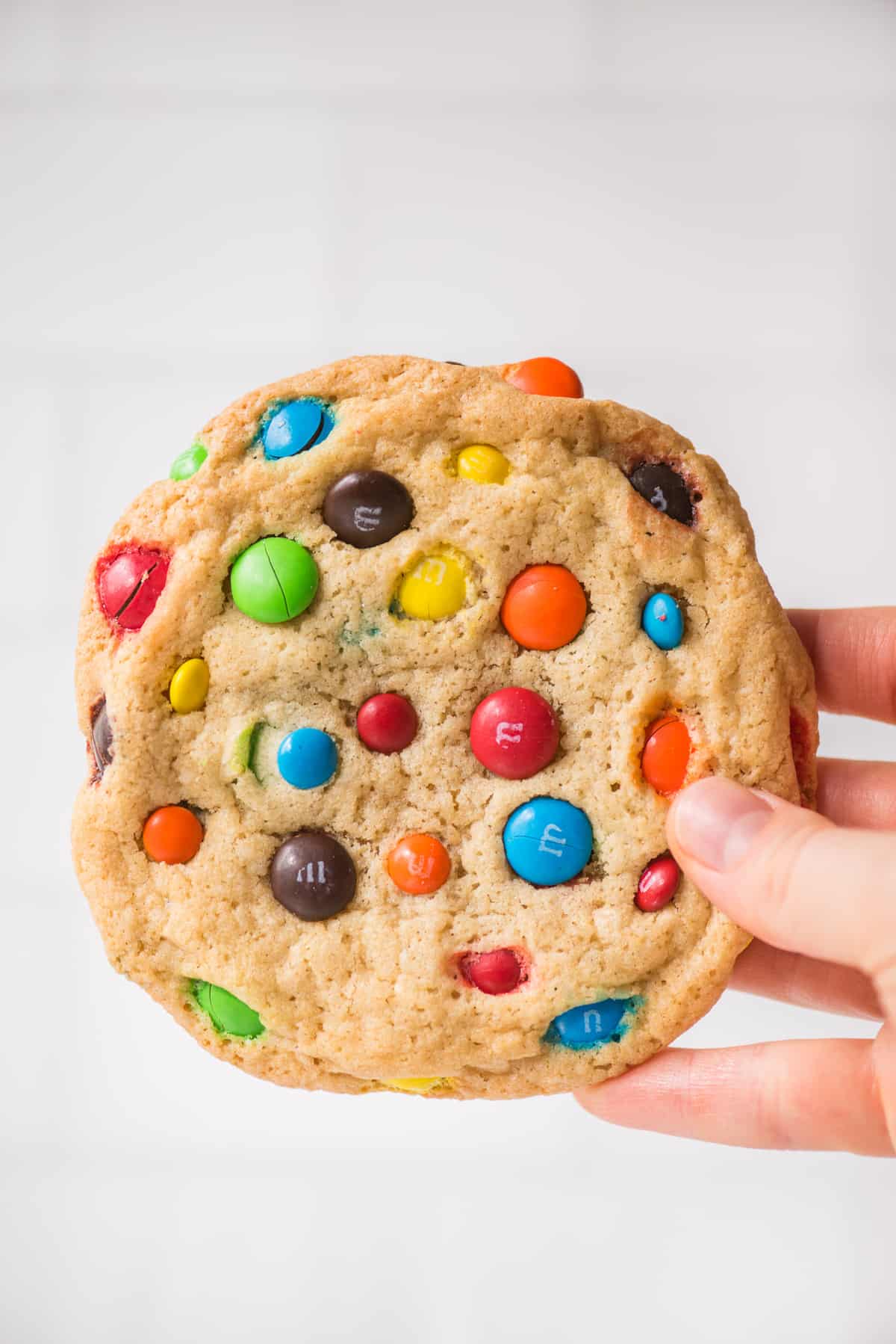 hand holding M&M cookie on white background