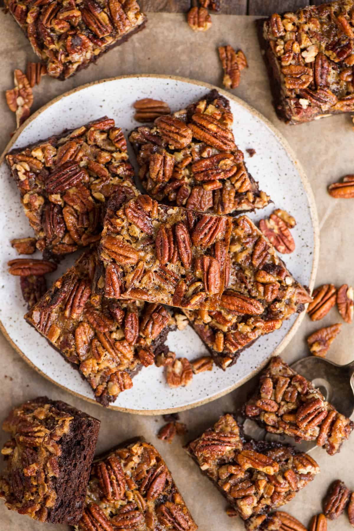 pecan pie brownies cut into squares and stacked on a white plate on a wooden background