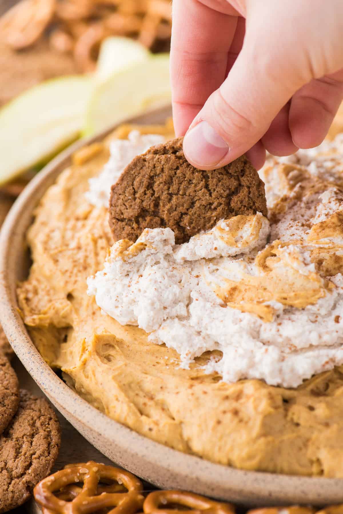 pumpkin dip with whipped cream topping in a bowl with hand dipping gingersnap cookie into dip