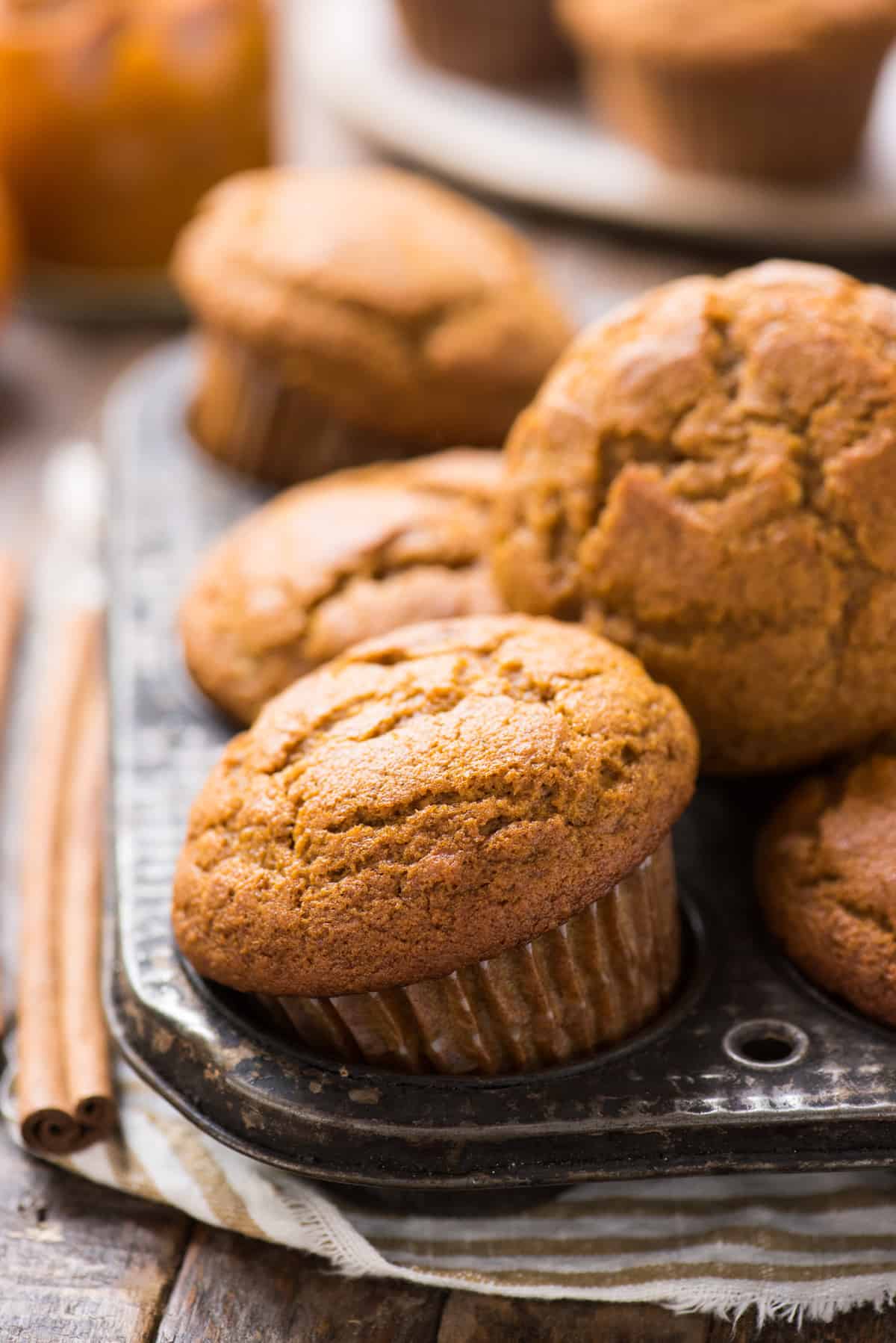 pumpkin muffins arranged in metal muffin pan with cinnamon stick on the left side