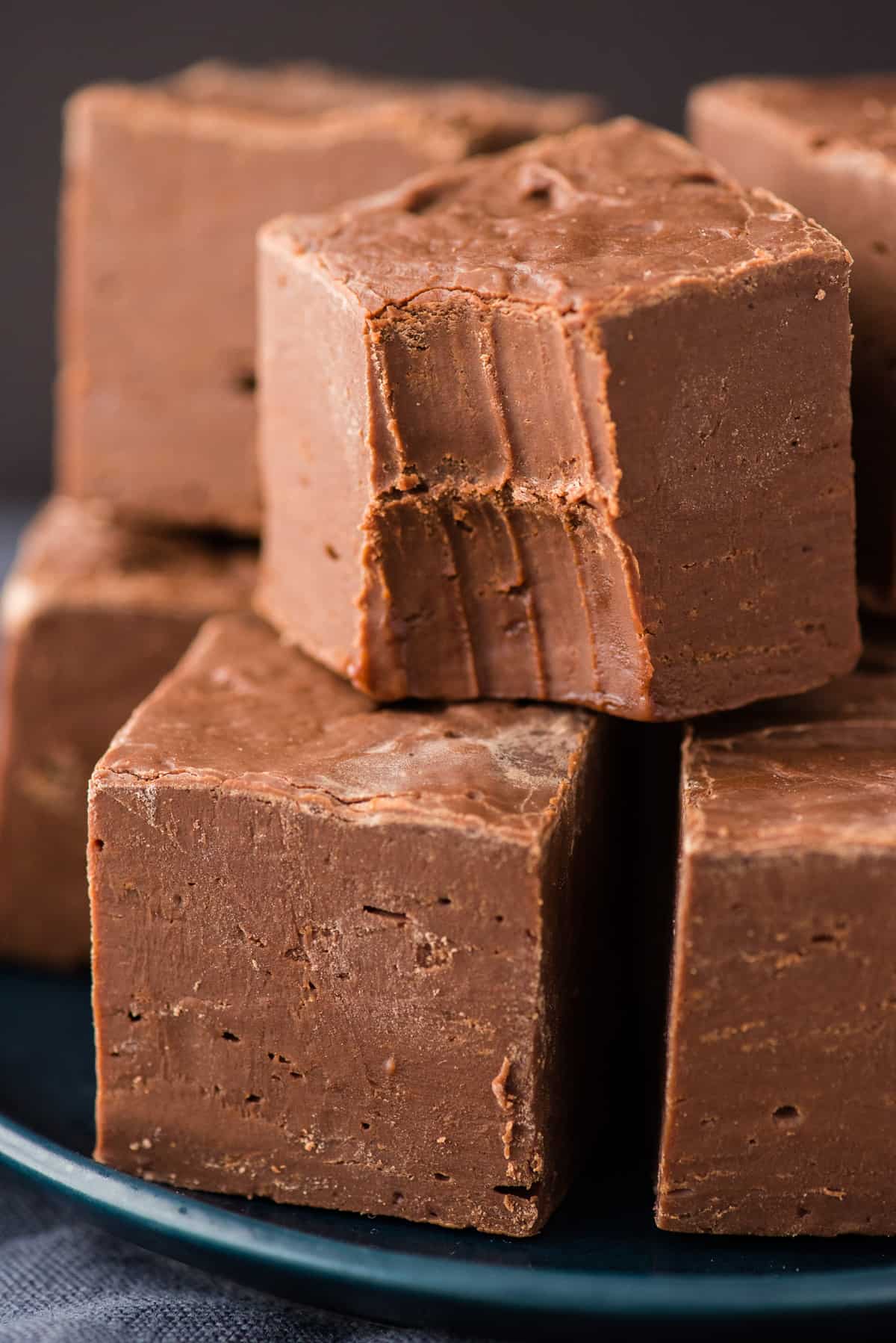 chocolate fudge cut into squares stacked on navy blue with black background