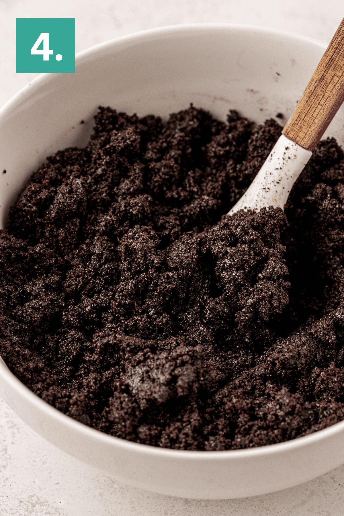 A white bowl filled with dark, crumbly Oreo pie crust mixture is being stirred with a wooden spoon. A green square with the number 4 appears in the top left corner.