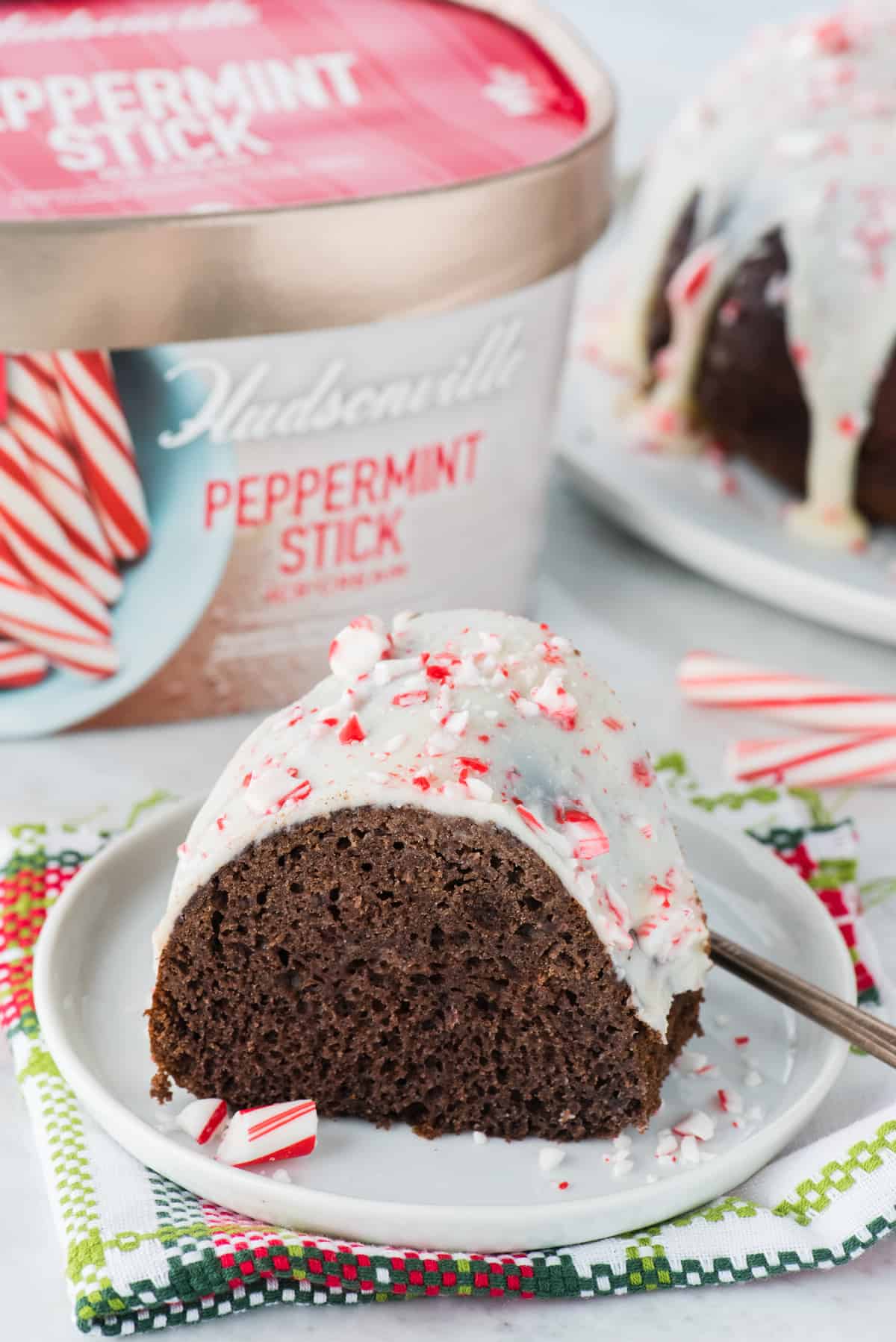 slice of chocolate peppermint bundt cake on white plate with ice cream container in the background