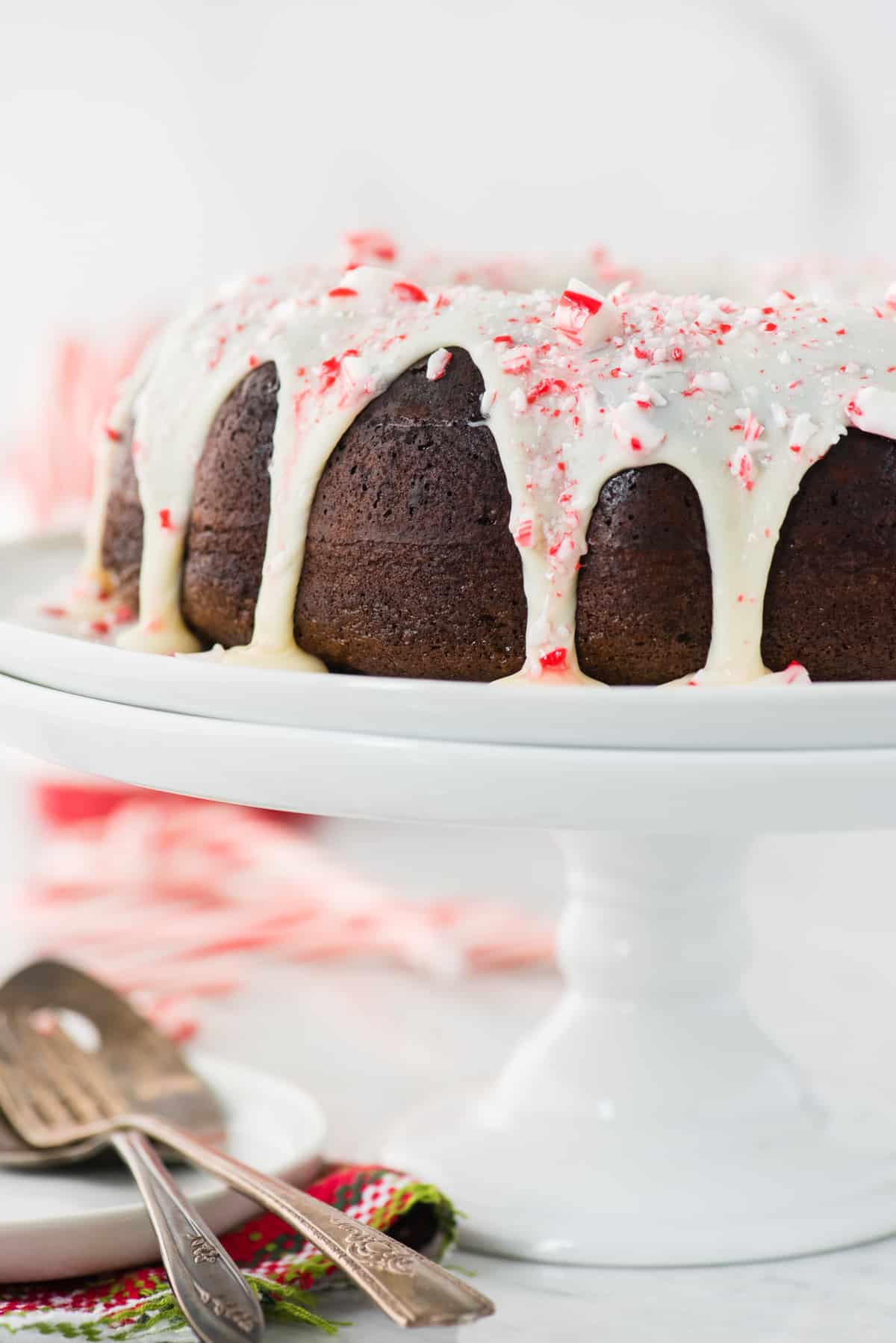 whole chocolate bundt cake with white chocolate glaze and candy cane pieces on white cake stand