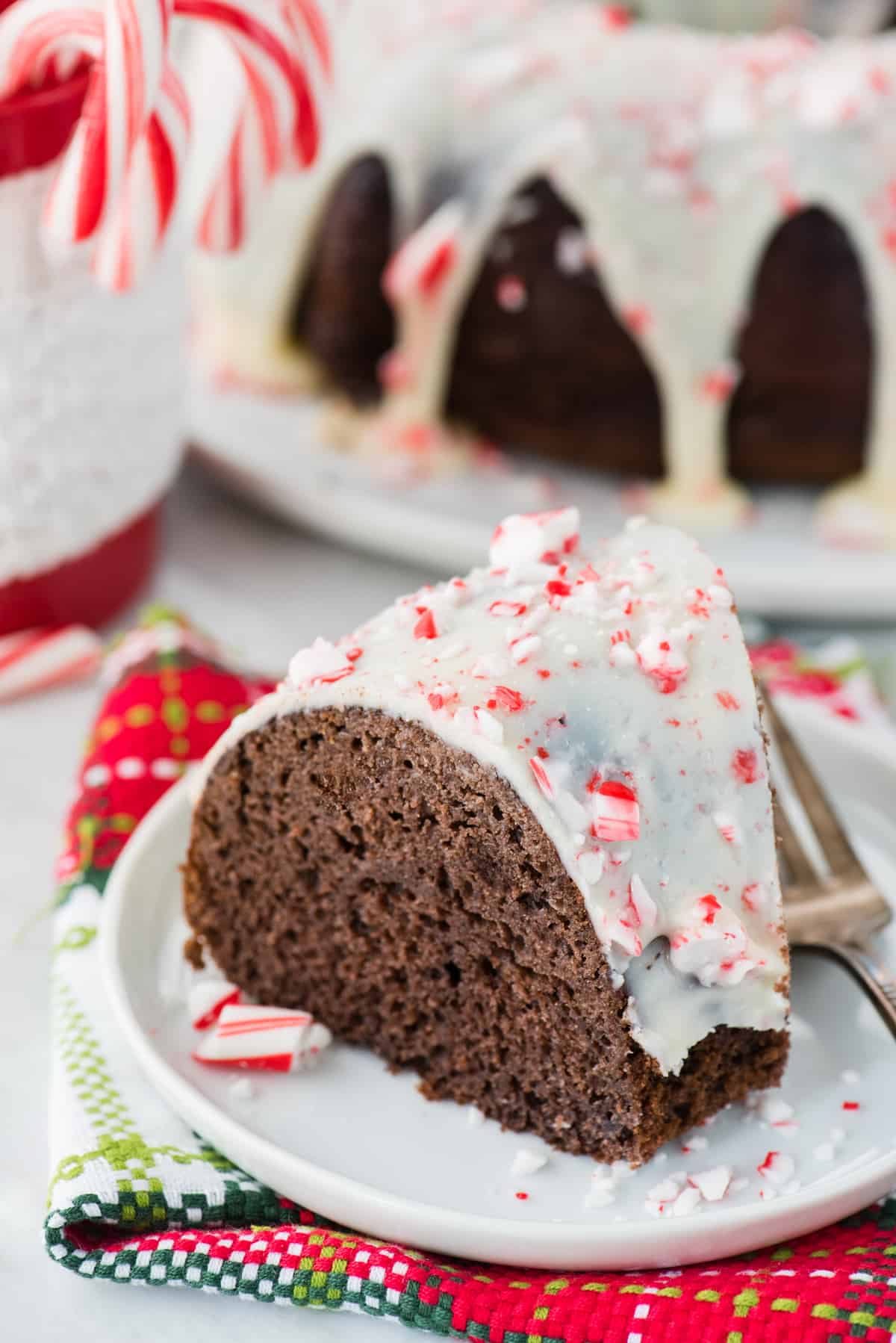 slice of chocolate peppermint bundt cake on white plate with candy canes in the background