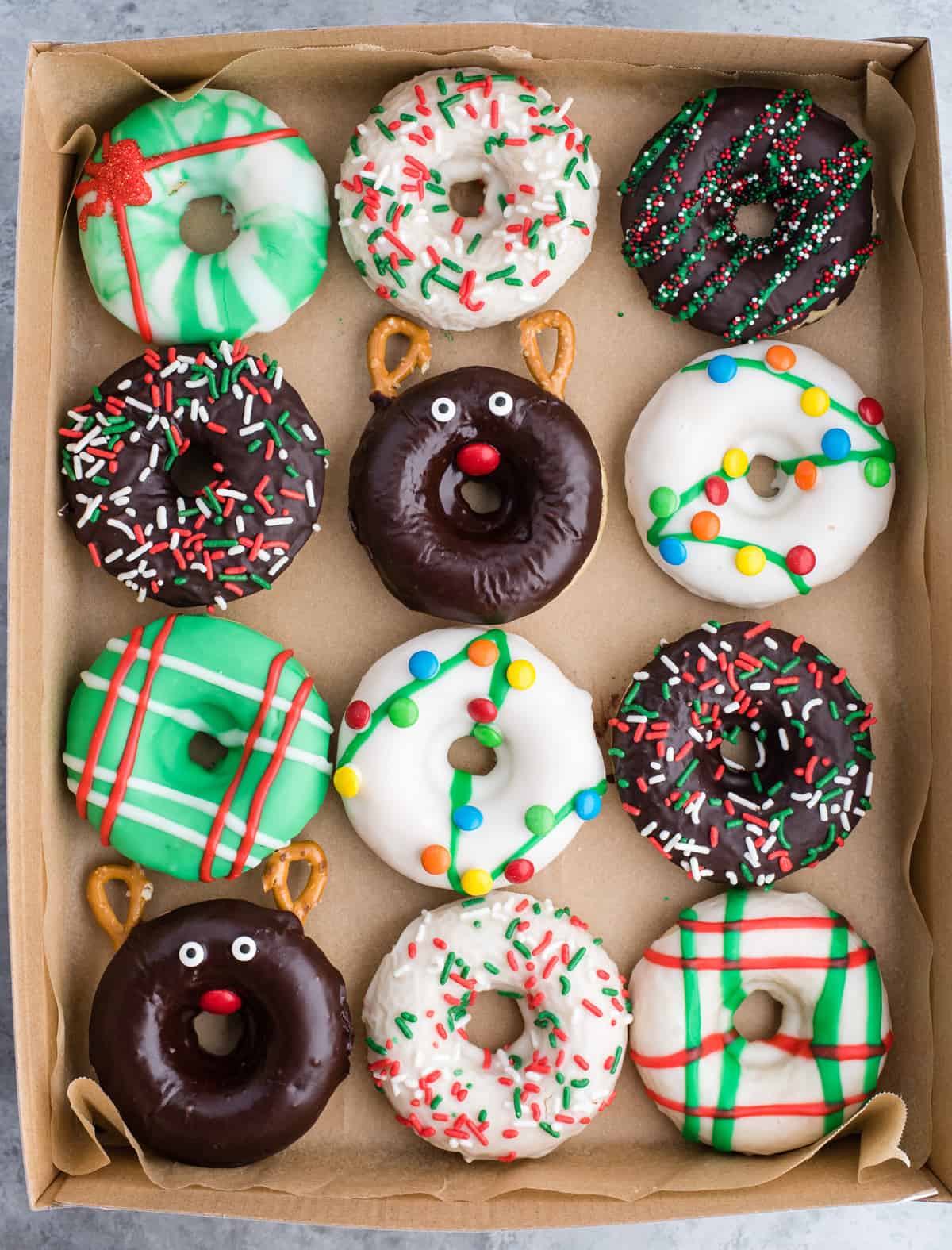 12 Christmas donuts arranged in a grid in a donut box