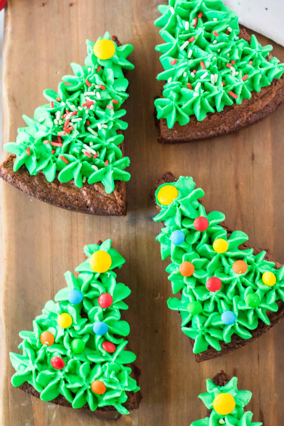 brownies cut into triangles and frosted with green frosting and sprinkles to look like Christmas trees on wooden background