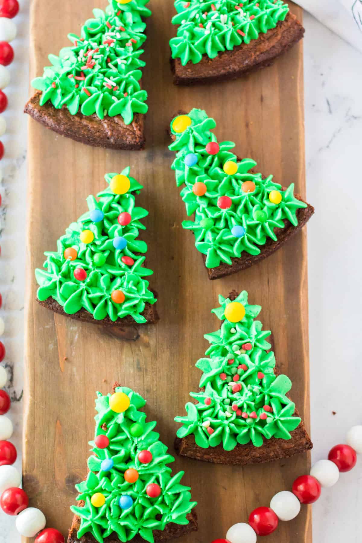 brownies cut into triangles and frosted with green frosting and sprinkles to look like Christmas trees on wooden background