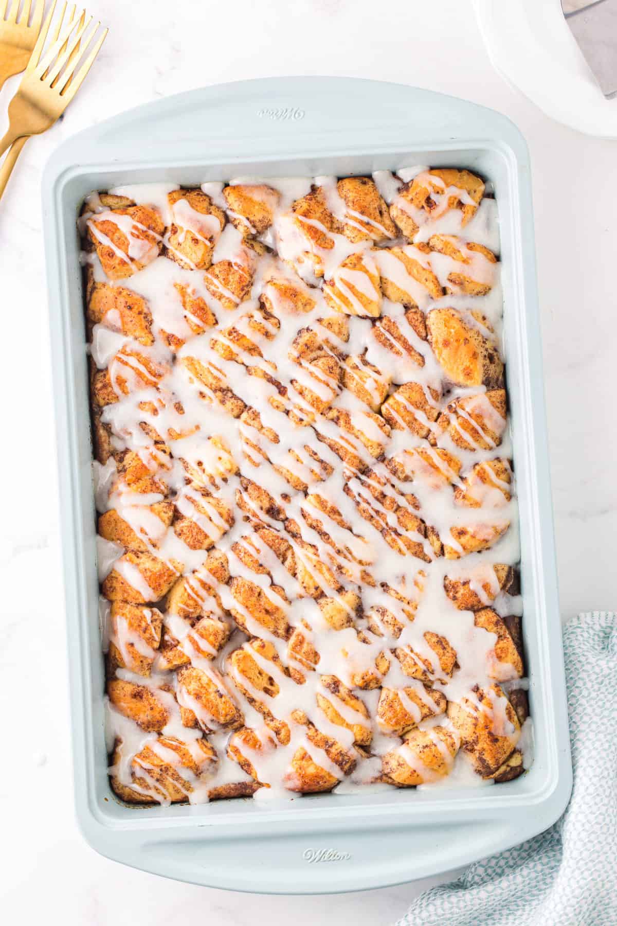 cinnamon roll casserole with icing drizzled on top in light blue baking dish