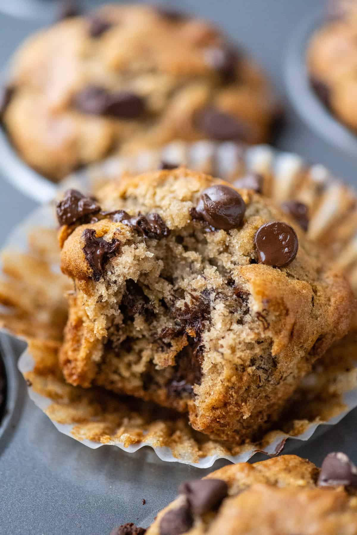 gluten free banana muffin with bite removed propped up in metal muffin pan