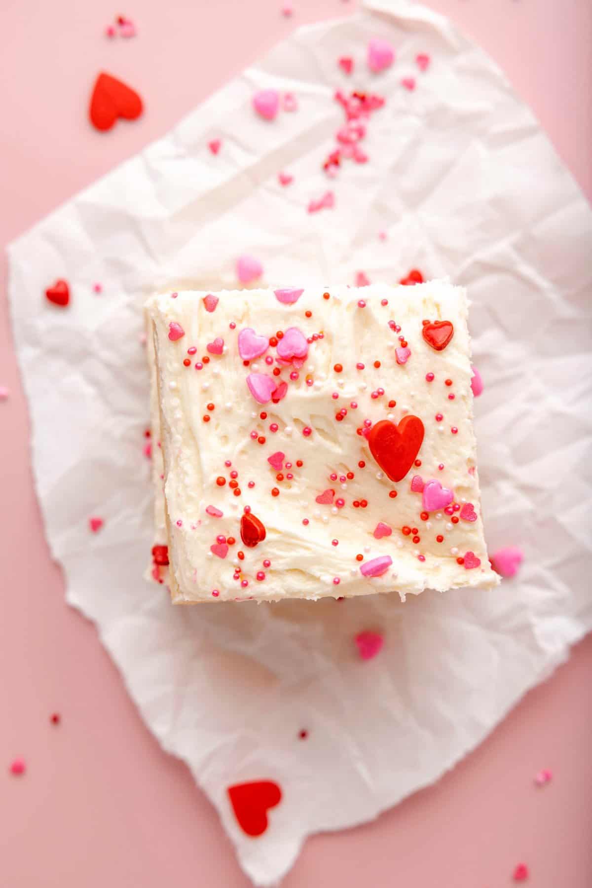 two sugar cookie bars with white frosting and valentine’s sprinkles on pink background
