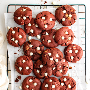 red velvet cookies with white chocolate chips scattered on top of a wire rack covered in parchment paper