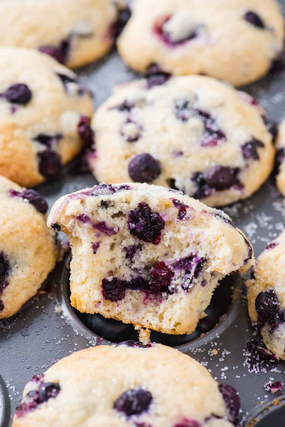 bite removed from blueberry muffin that’s sitting in metal muffin pan