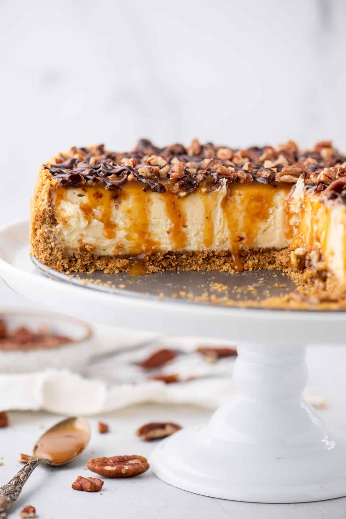 turtle cheesecake on white cake stand with slice removed