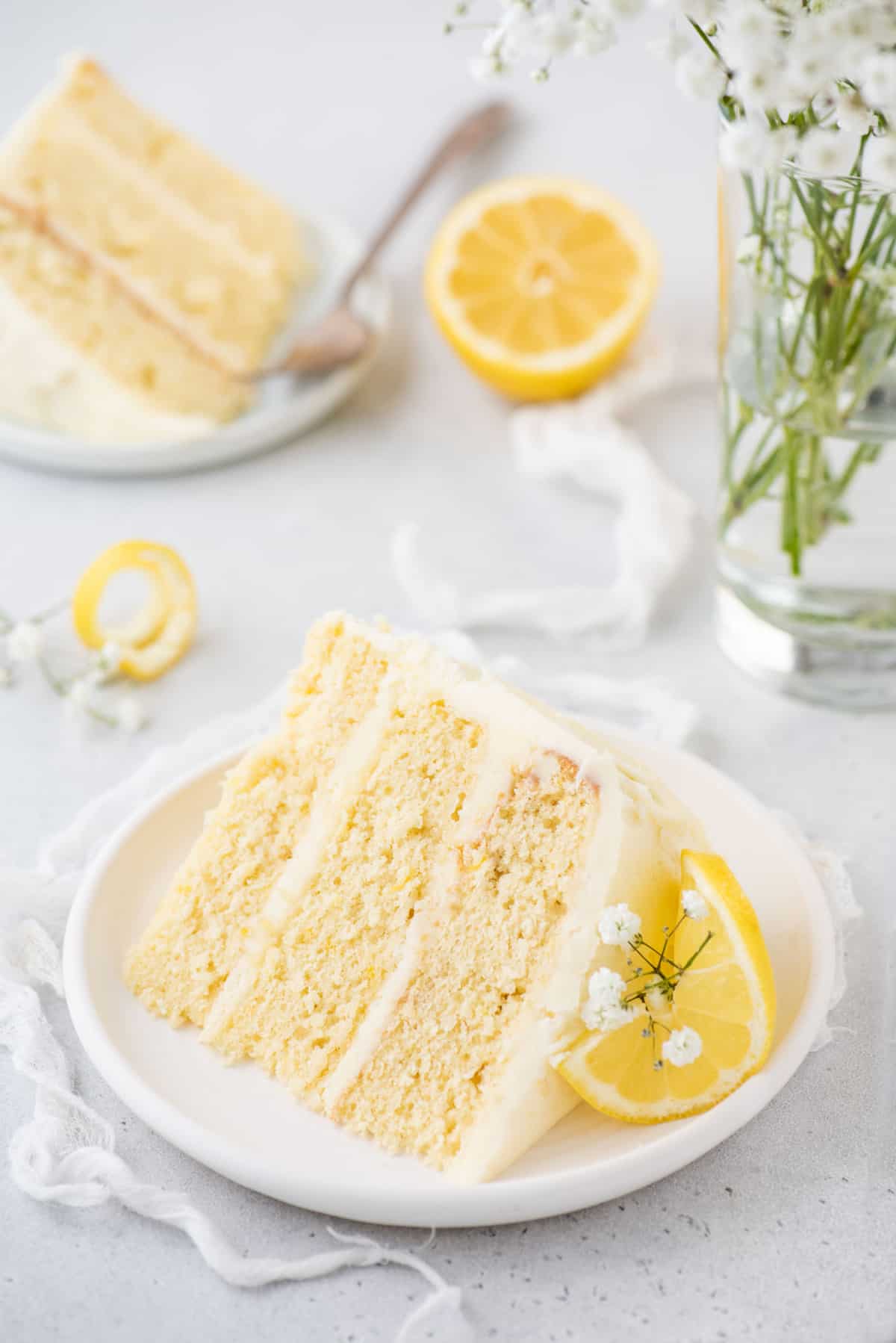 Two plates of three-layer lemon cake garnished with baby's breath and lemon slices