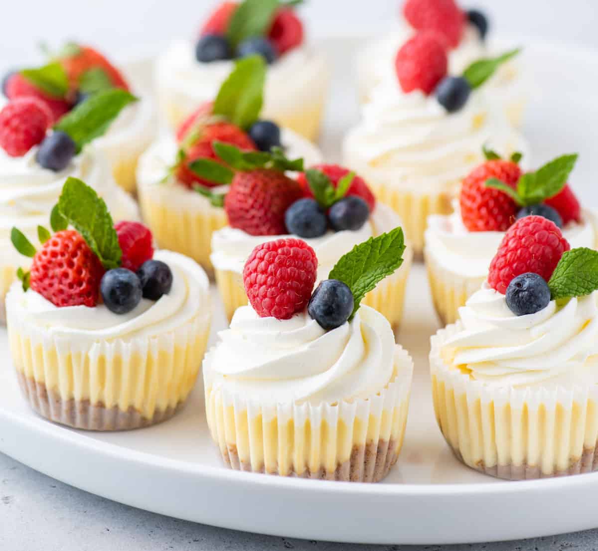 Serving tray of mini cheesecakes garnished with whipped cream, fresh berries, and mint leaves