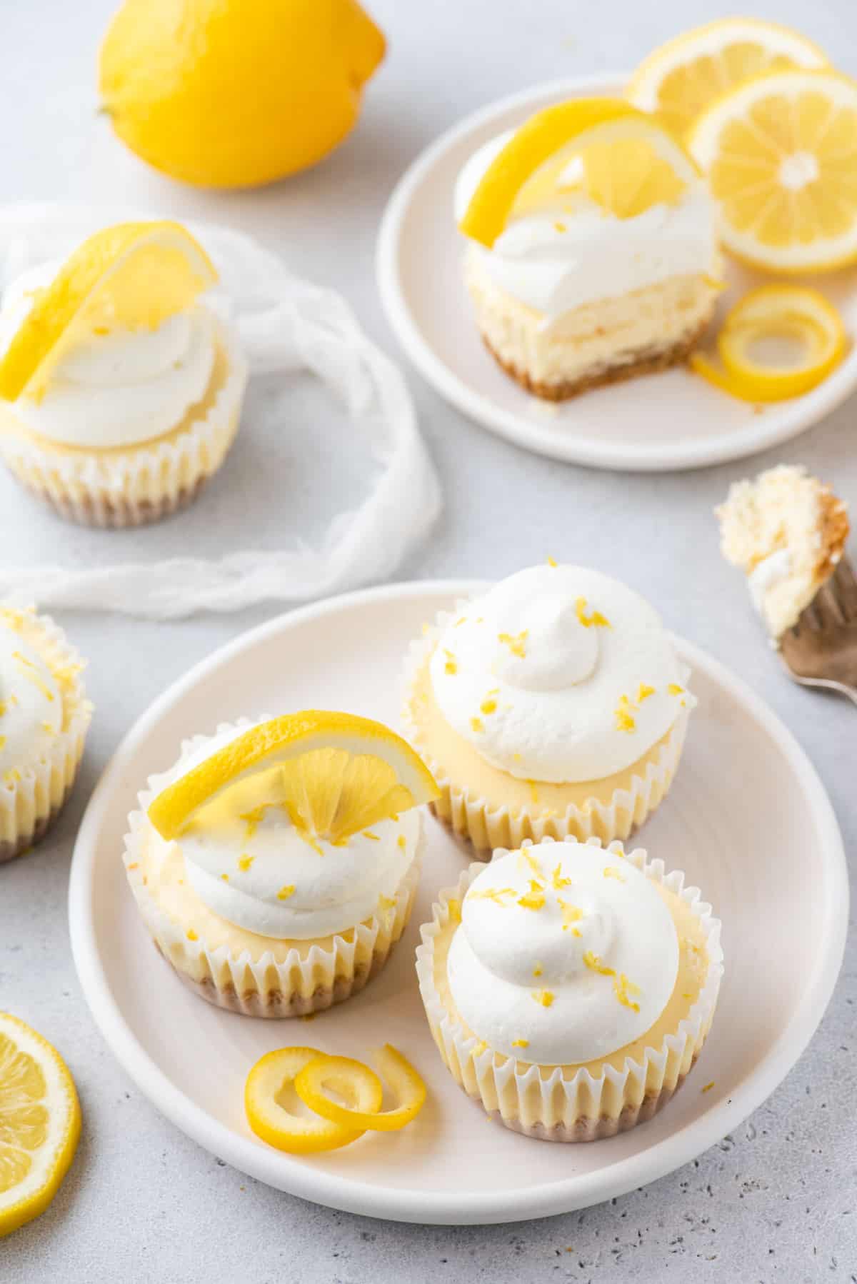 Mini lemon cheesecakes topped with whipped cream and lemon zest arranged on white plates