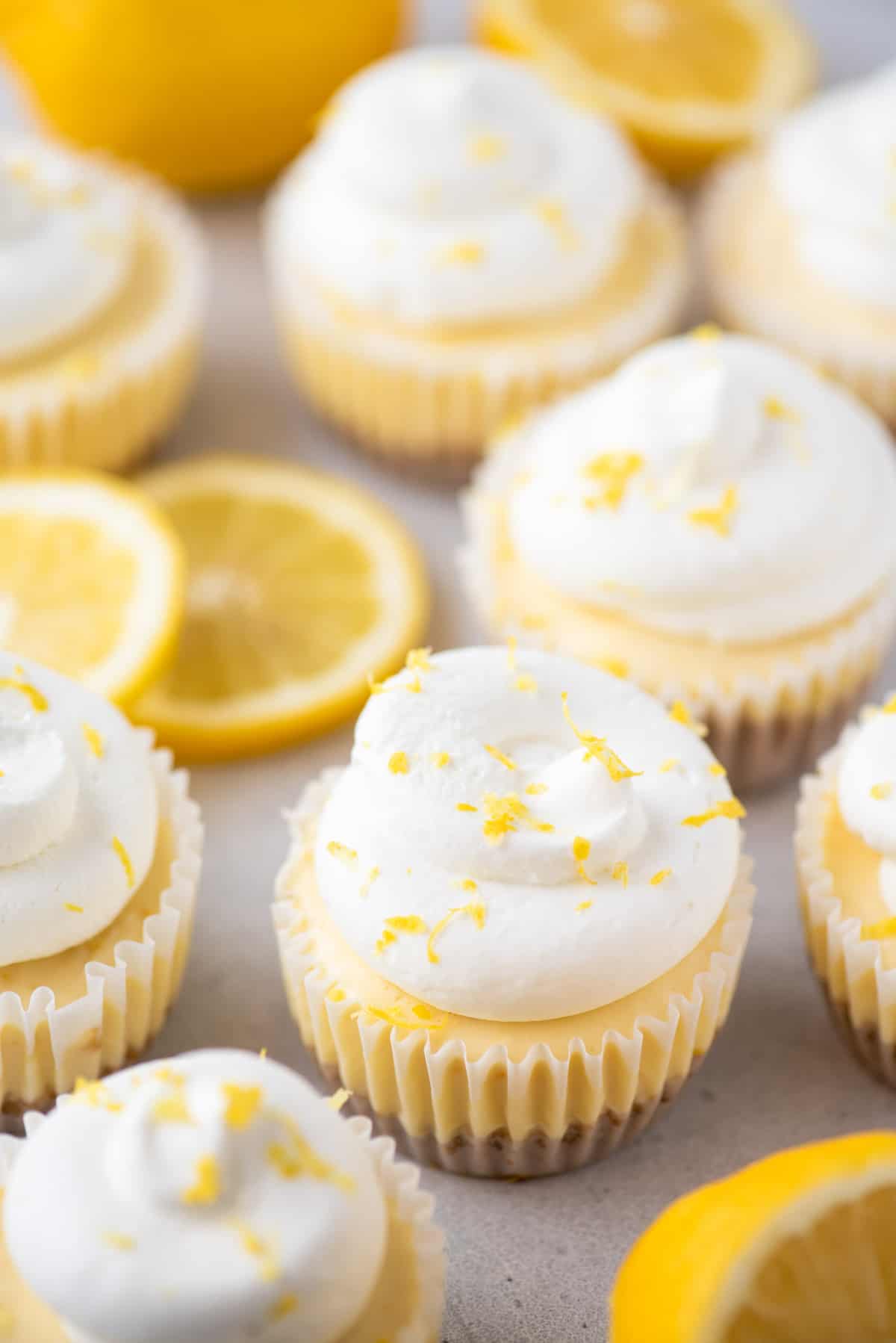 Mini lemon cheesecakes topped with whipped cream and lemon zest arranged on white surface