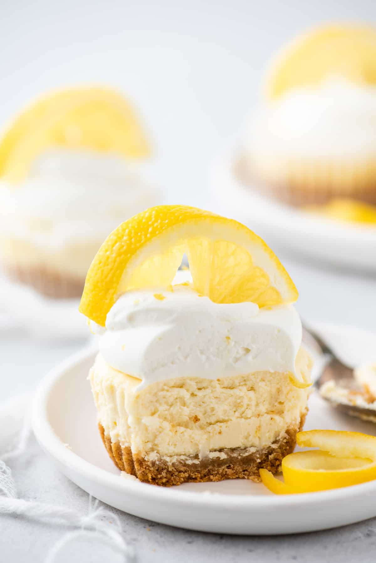 Mini lemon cheesecake topped with whipped cream and lemon slice with bite removed on white plate