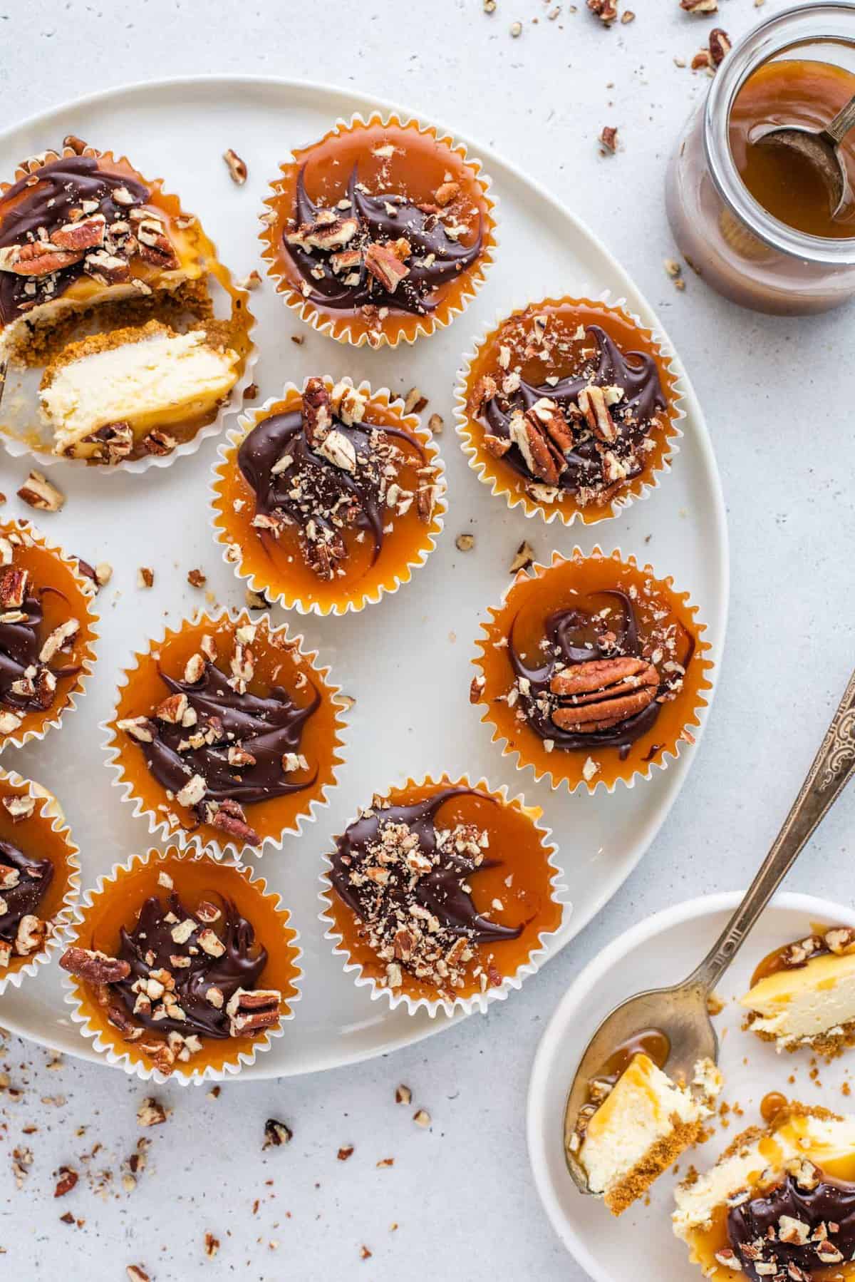 mini cheesecakes topped with caramel, chocolate and chopped pecans arranged on white tray
