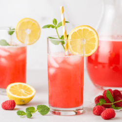 Glass of raspberry lemonade with ice cubes, paper straw, sprig of mint, and lemon slice