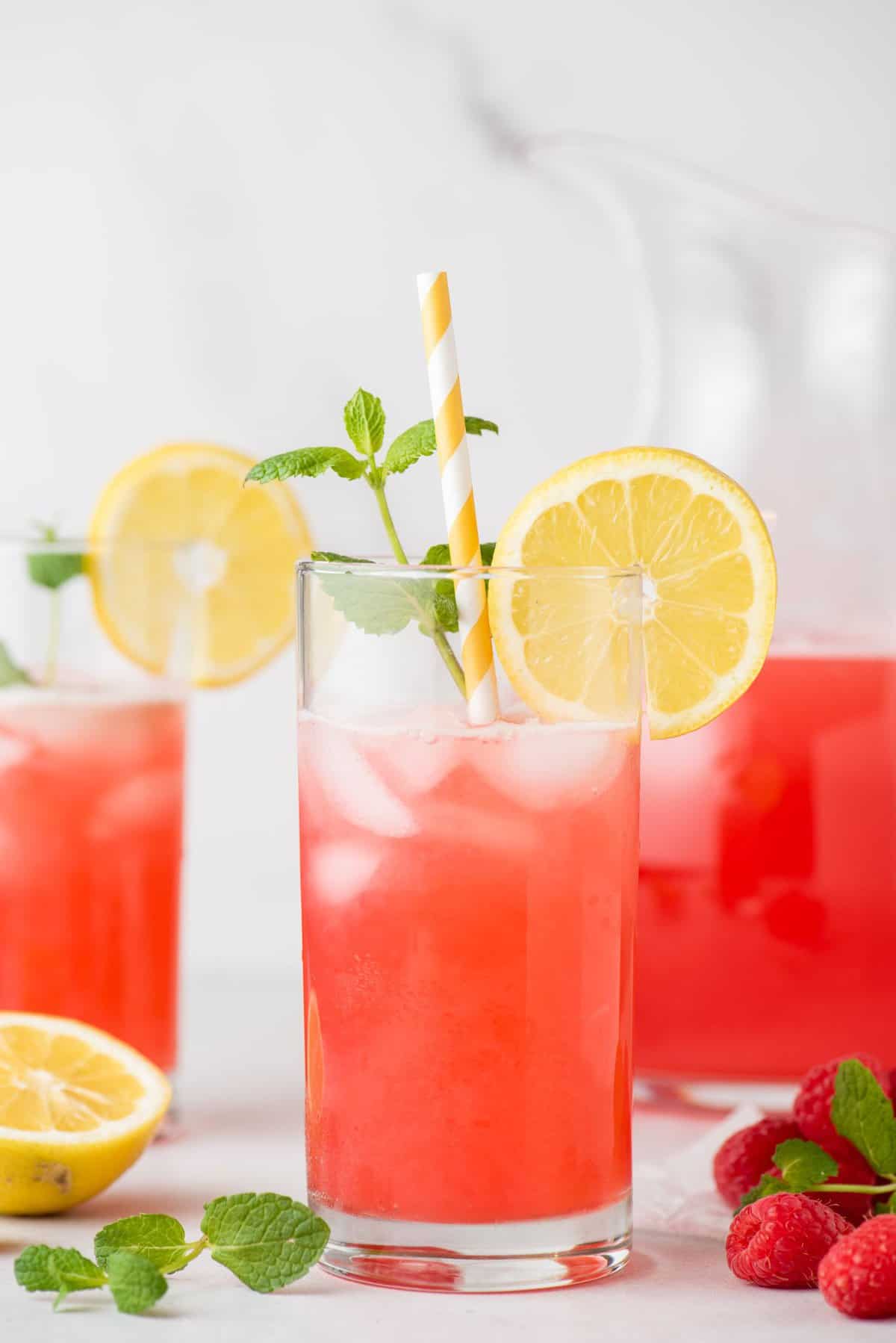 Glass of raspberry lemonade garnished with sliced lemon, mint leaves, and striped paper straw