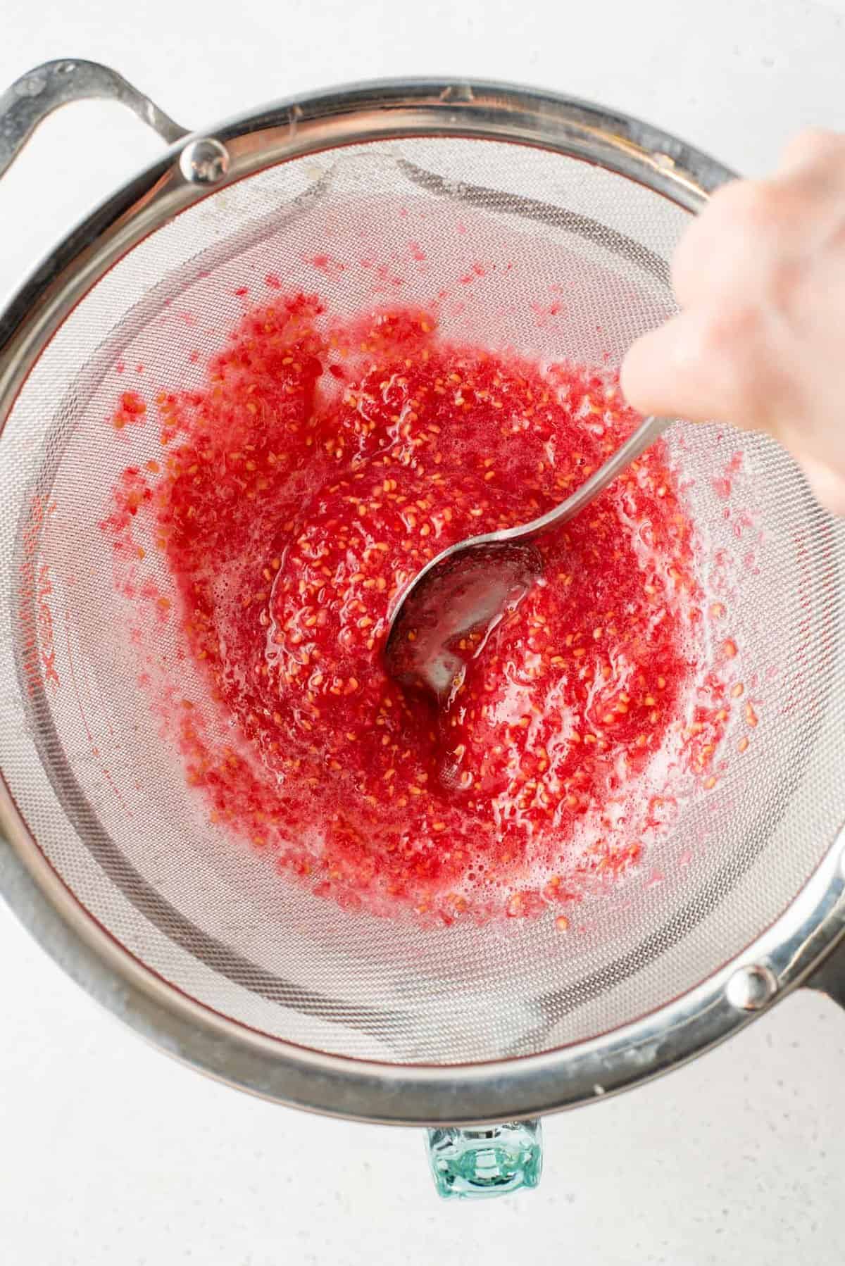 Using spoon to smash raspberry puree through fine mesh sieve