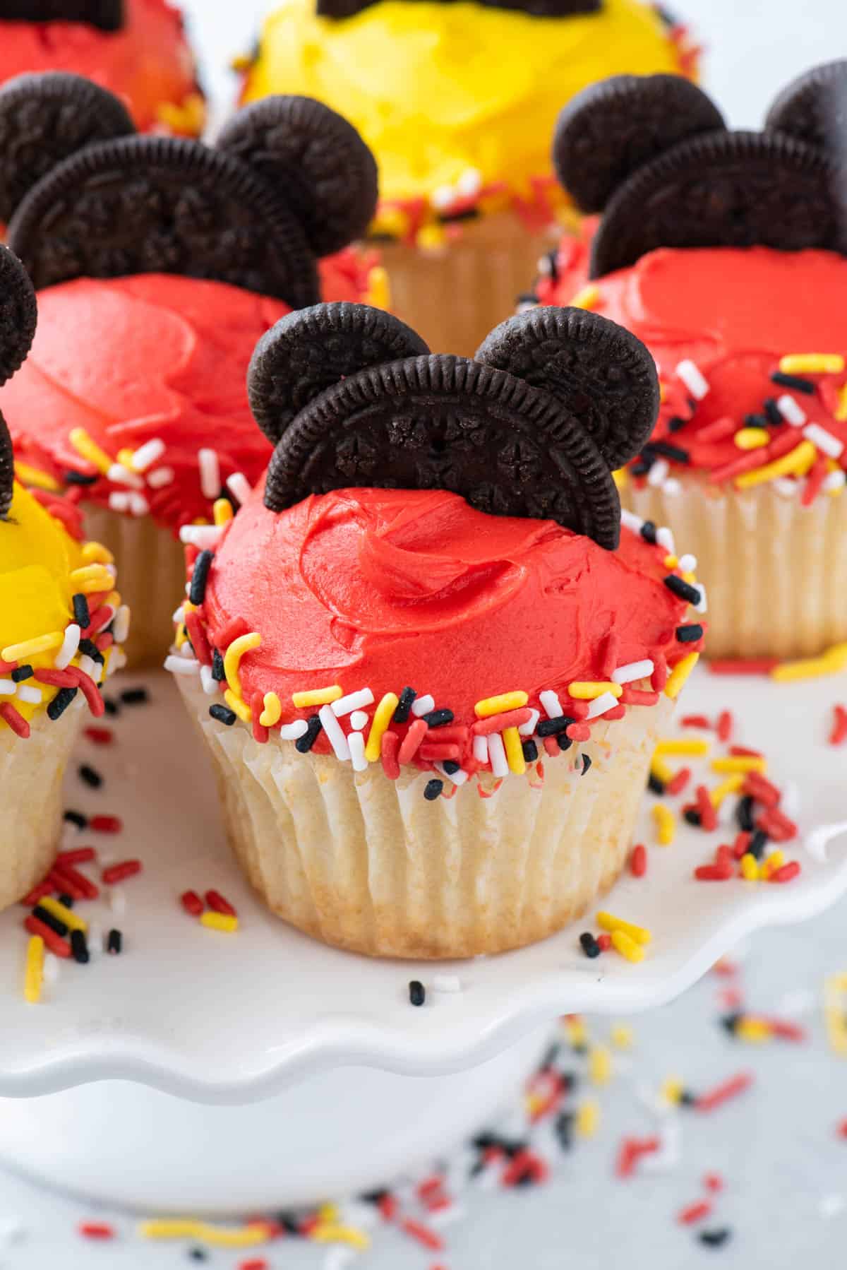 Mickey Mouse cupcakes on cake stand with sprinkles scattered around them