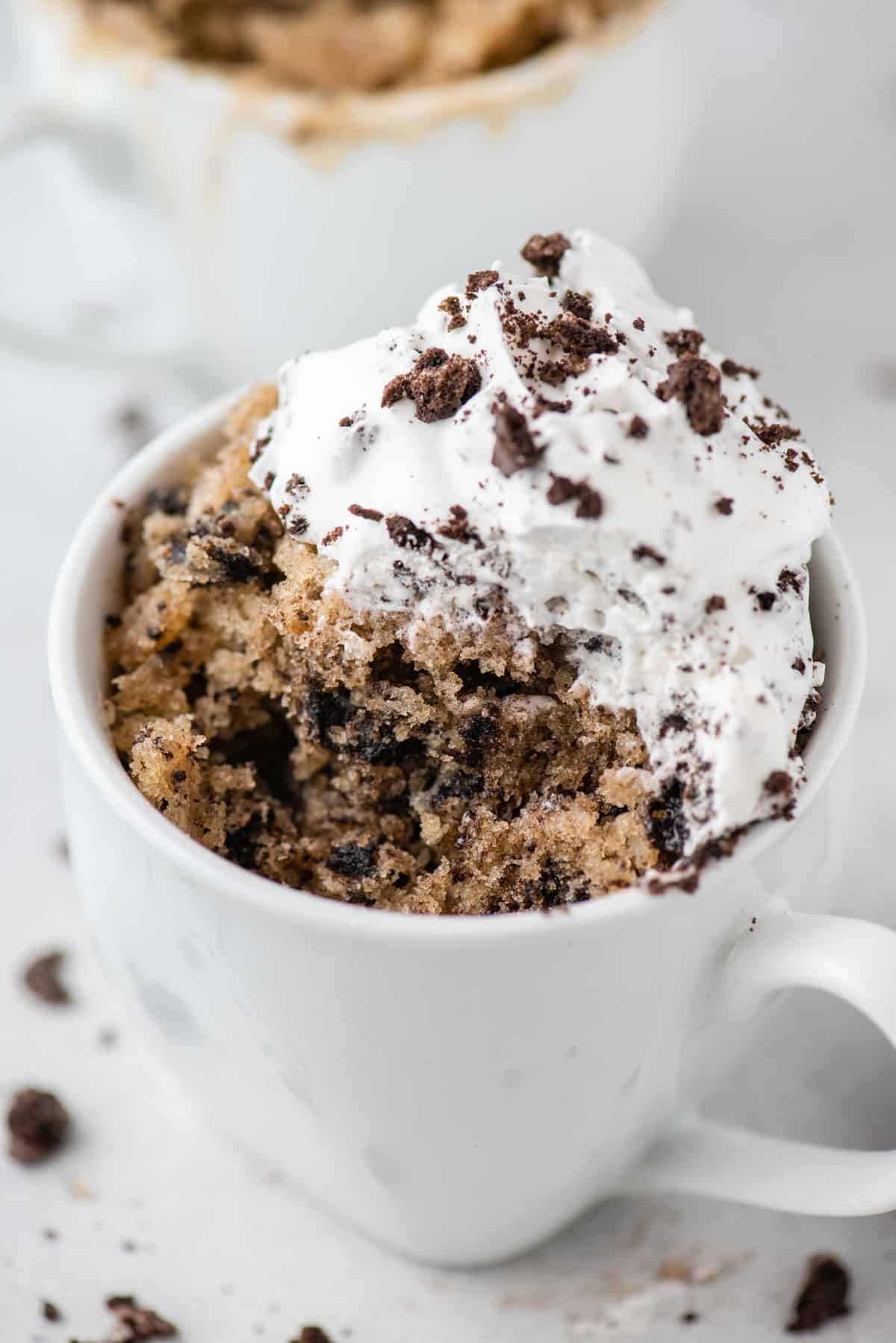 Oreo mug cake in white mug, topped with whipped cream and crushed Oreos