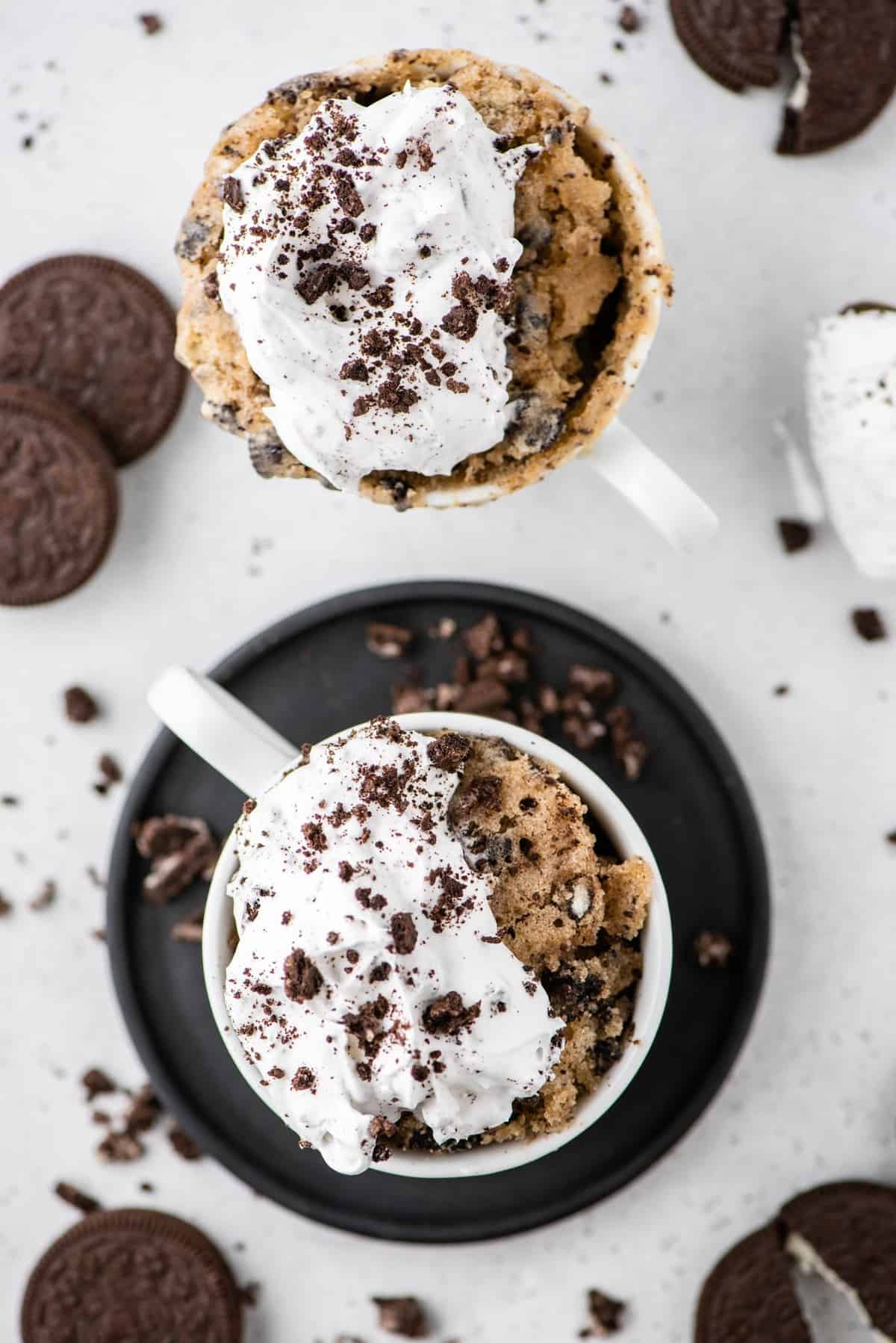 Overhead view of two Oreo mug cakes topped with whipped cream and Oreo crumbs