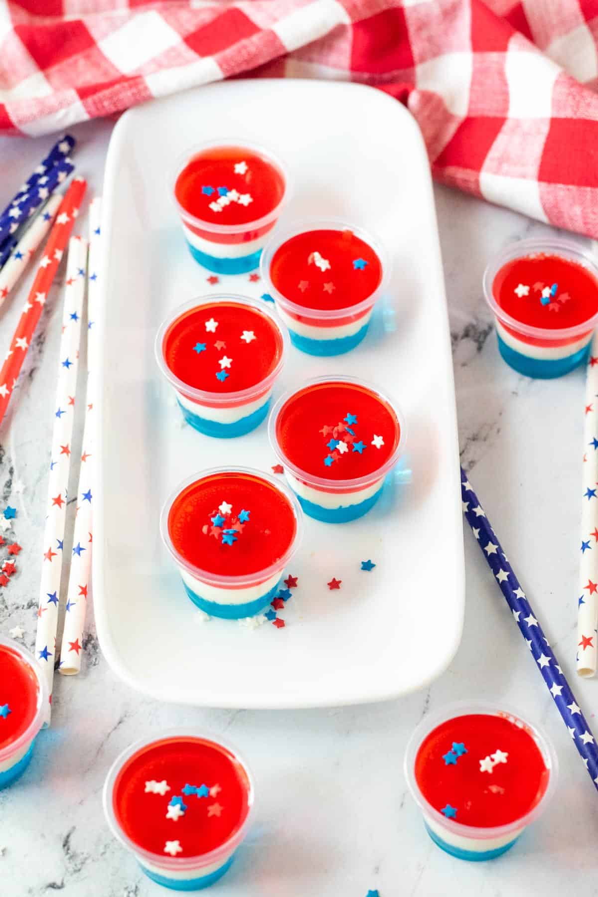 Red, white, and blue Jello shots on tray and marble counter with festive straws