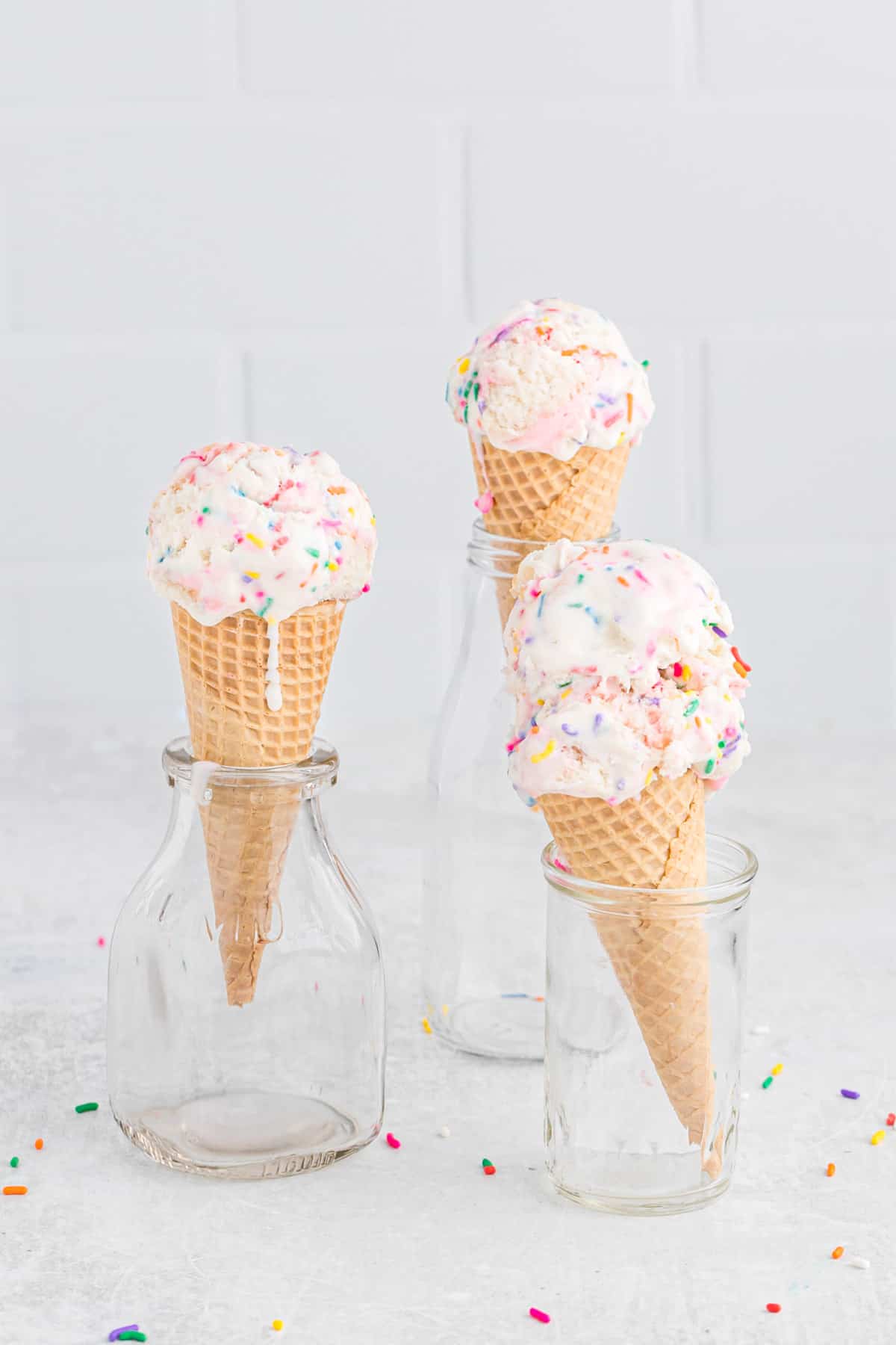 Three ice cream cones with birthday cake ice cream, set in glass jars to hold them upright