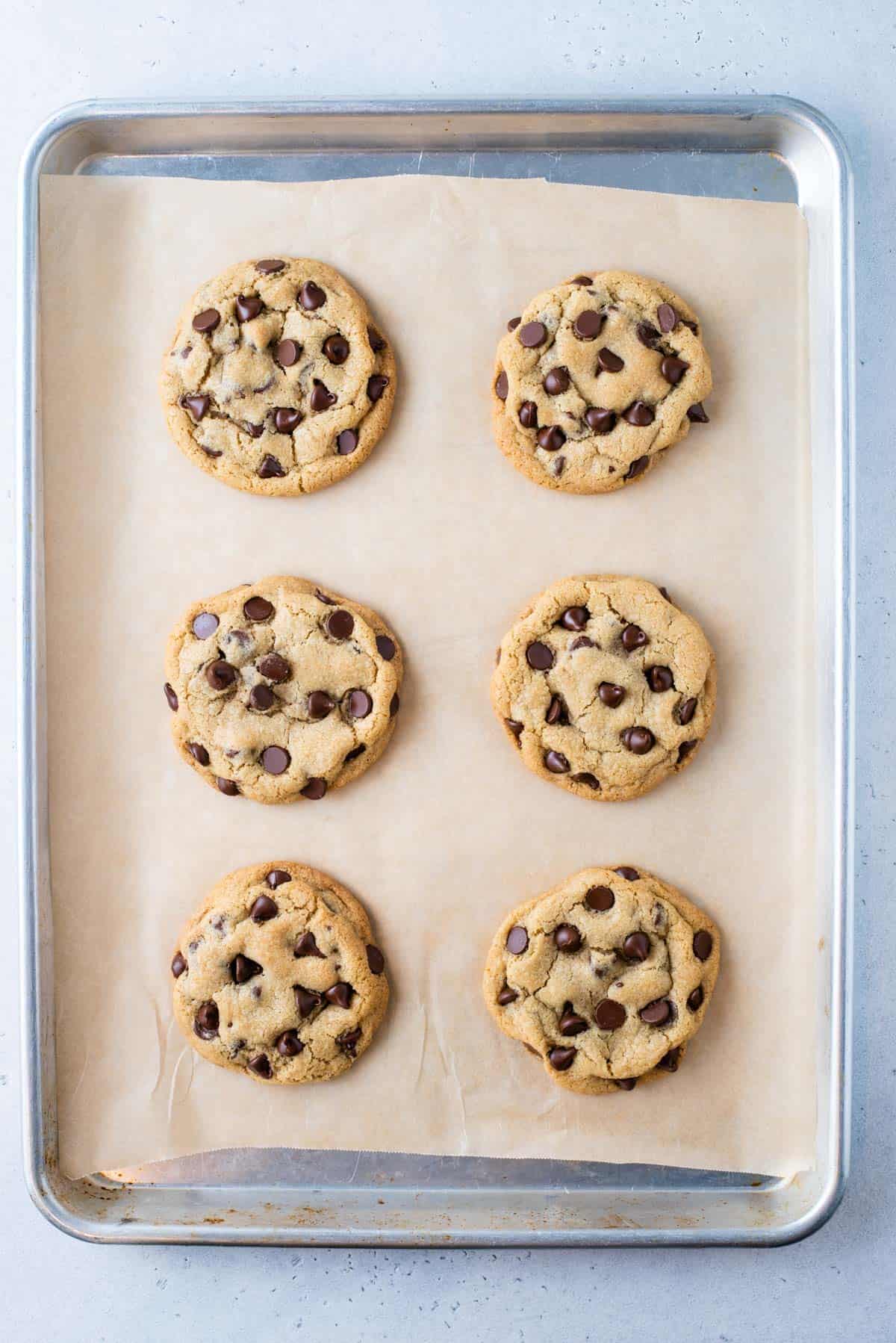 Overhead view of 6 chocolate chip cookies on parchment-lined baking sheet