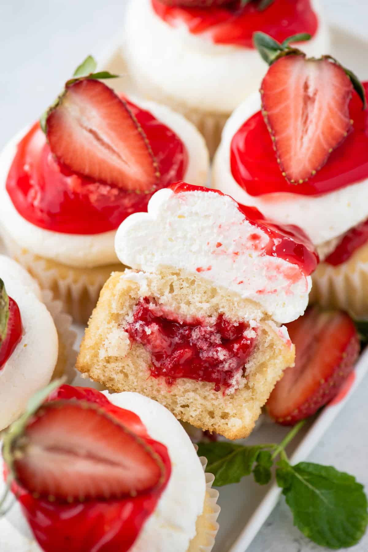 Strawberry shortcake cupcakes, with one cut in half to show filling