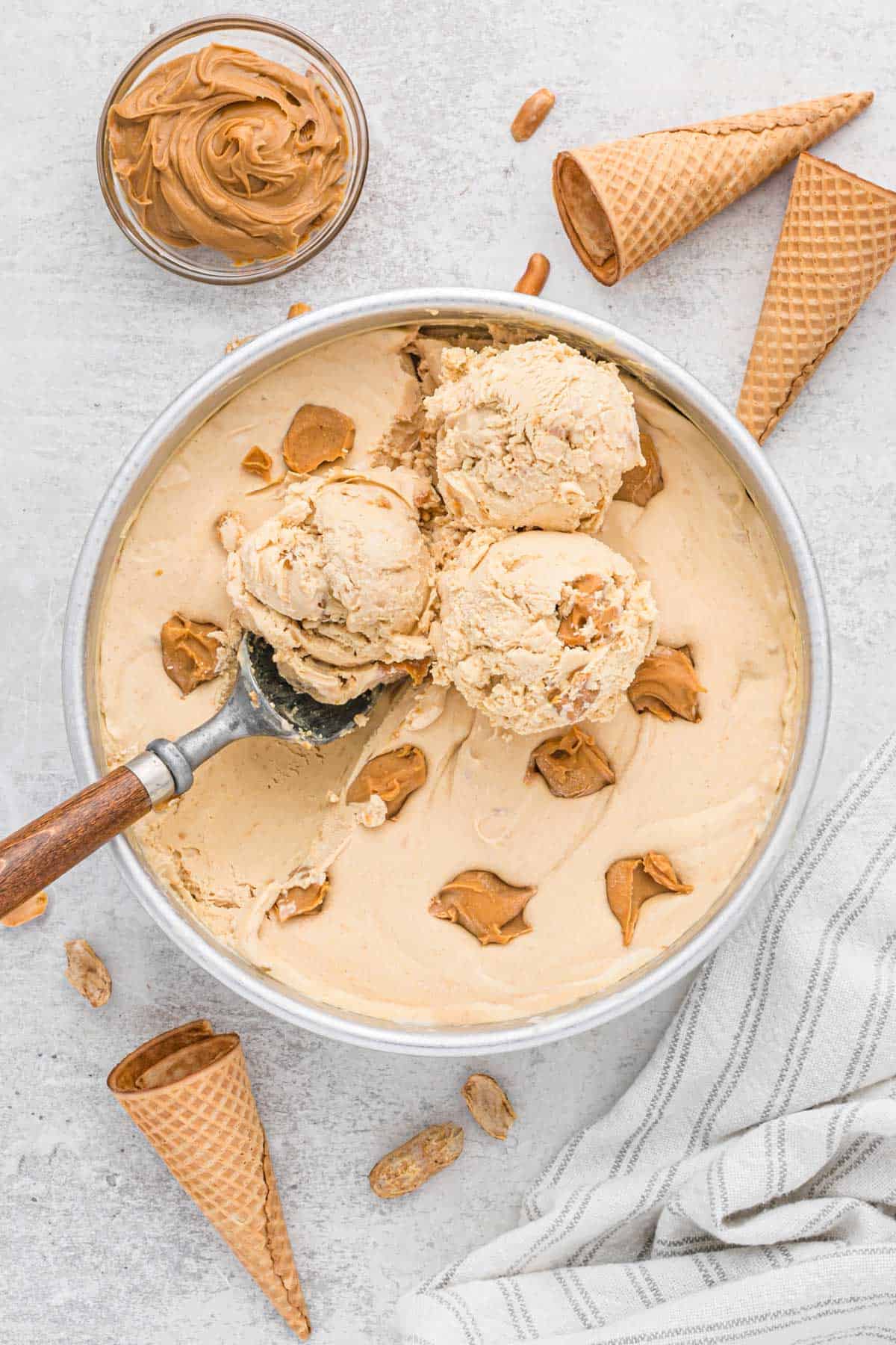 Overhead view of cake pan filled with peanut butter ice cream, surrounded by cones and a bowl of peanut butter