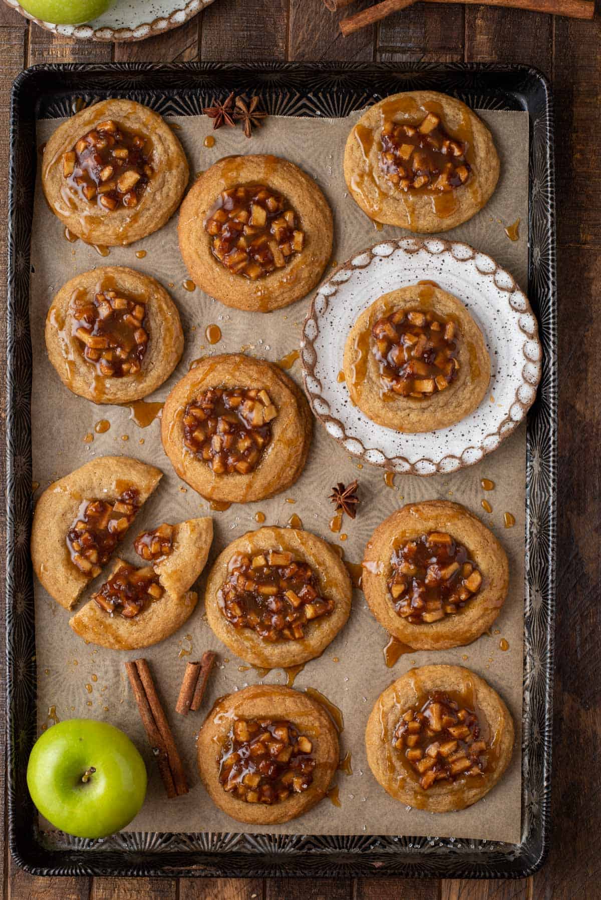 Overhead view of apple pie cookies on baking sheet, with one on plate