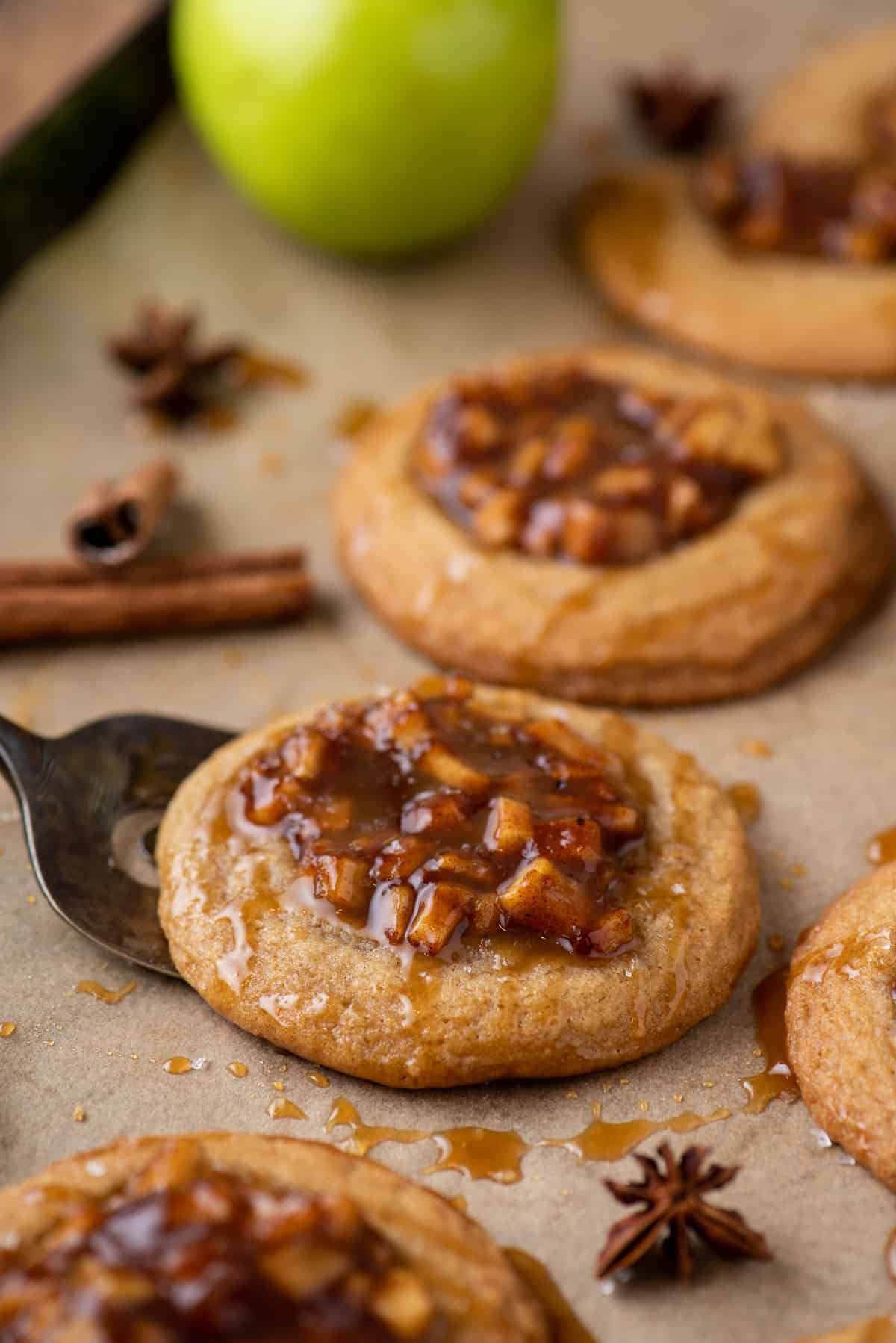 Apple pie cookies on baking sheet with one being lifted by spatula