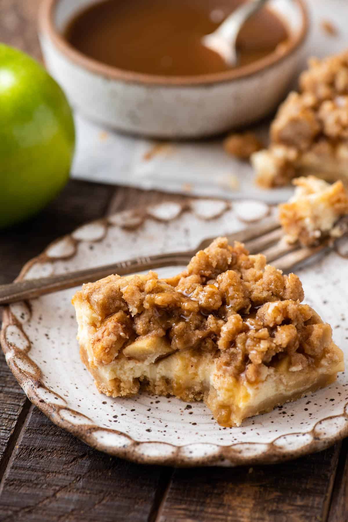 Caramel apple cheesecake bar on plate with bite taken out of corner