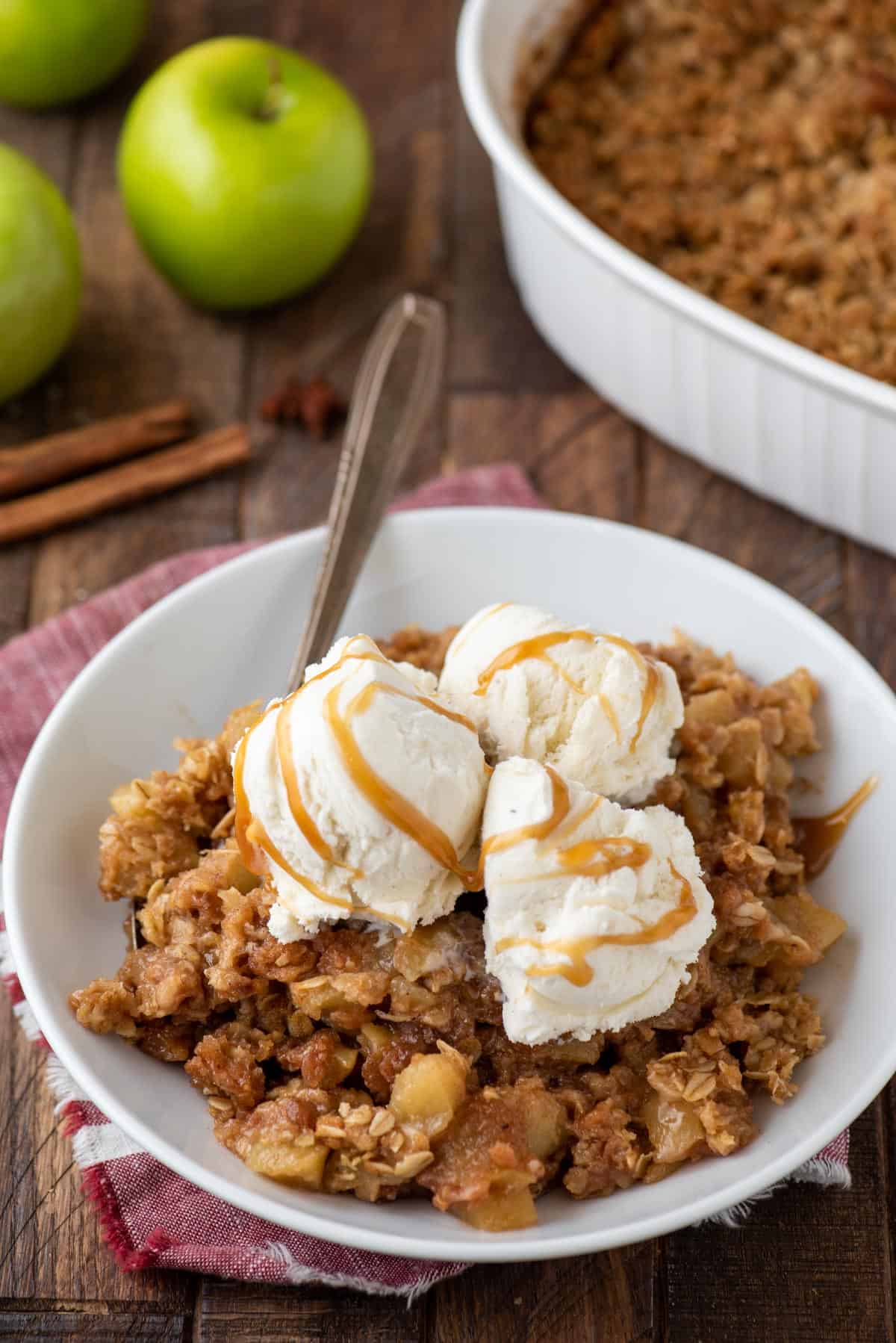 Caramel apple crisp in bowl topped with vanilla ice cream and caramel sauce