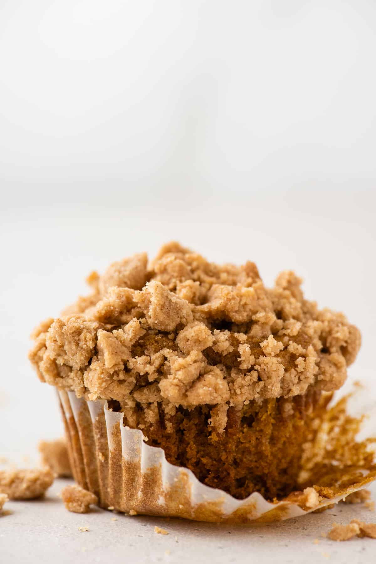 a single gluten free pumpkin muffin with liner half removed on white background