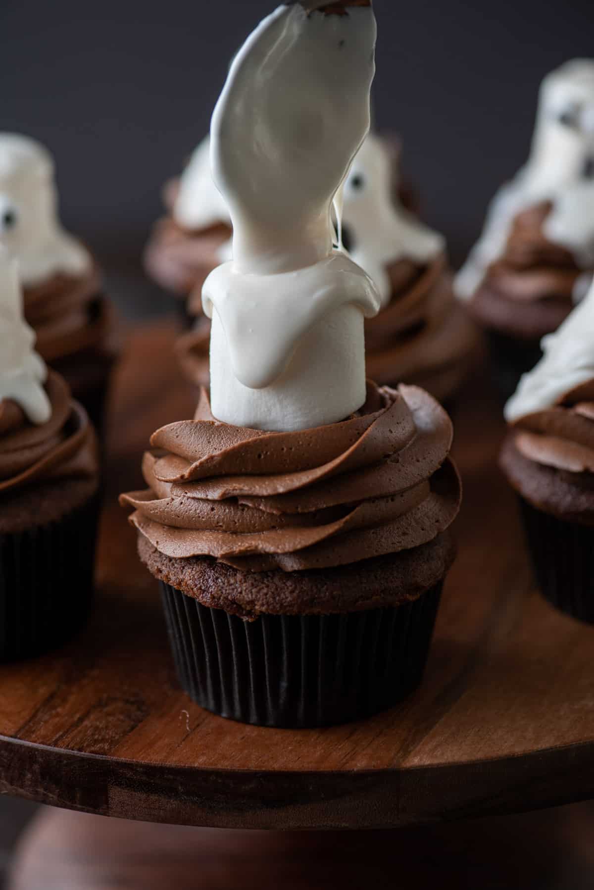 a spoon is drizzling melted white frosting over a large marshmallow that is on top of a chocolate cupcake
