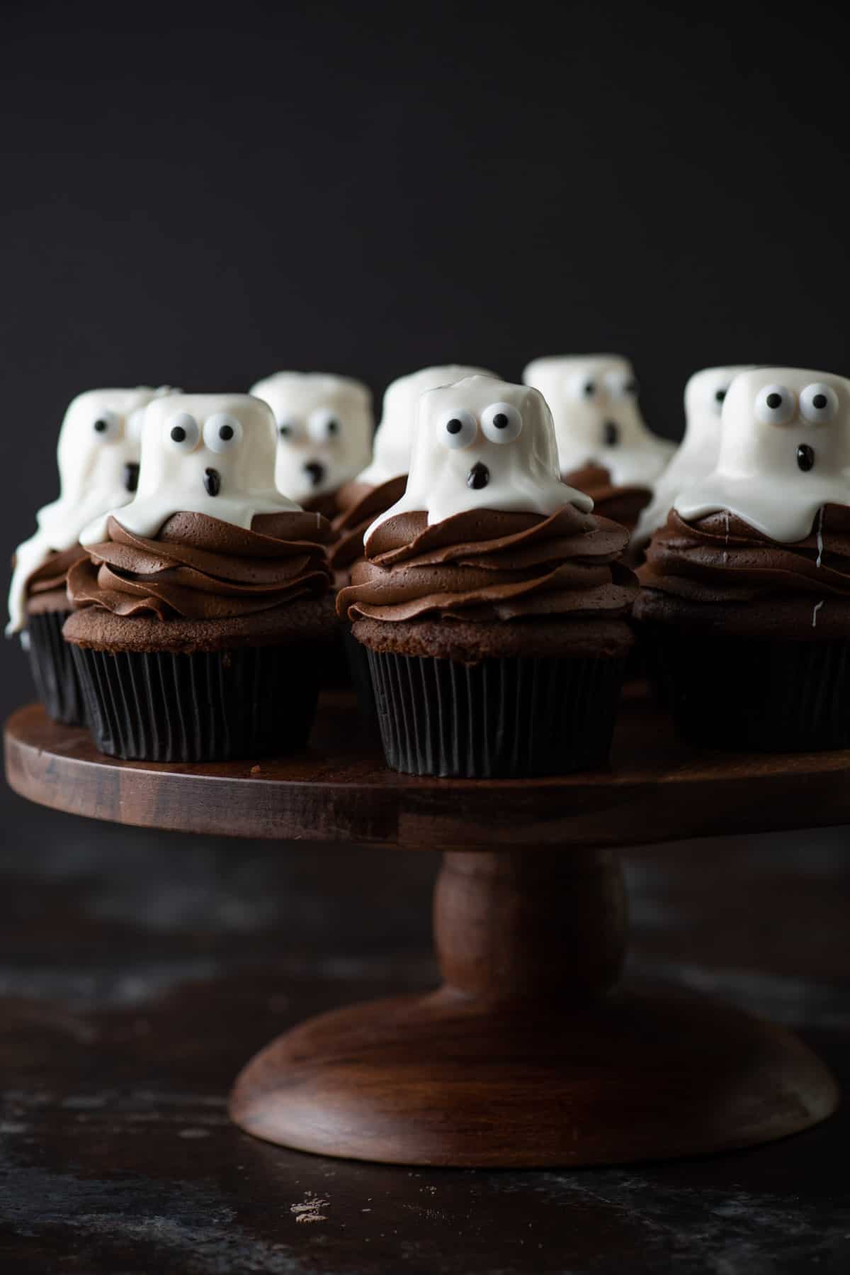 ghost cupcakes arranged on wooden cake stand on dark background