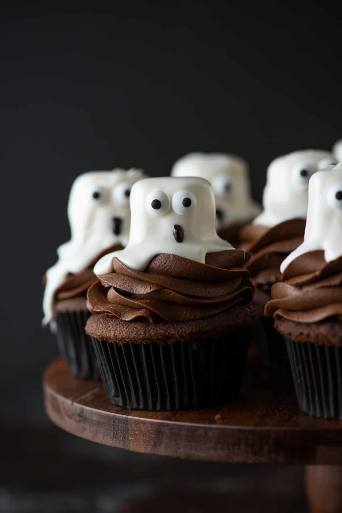 ghost cupcakes arranged on wooden cake stand on dark background